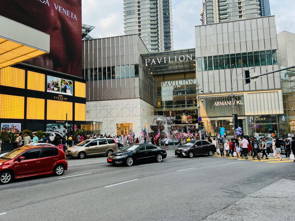 Vibrant street view of Pavilion Kuala Lumpur, showcasing urban life with cars and pedestrians.