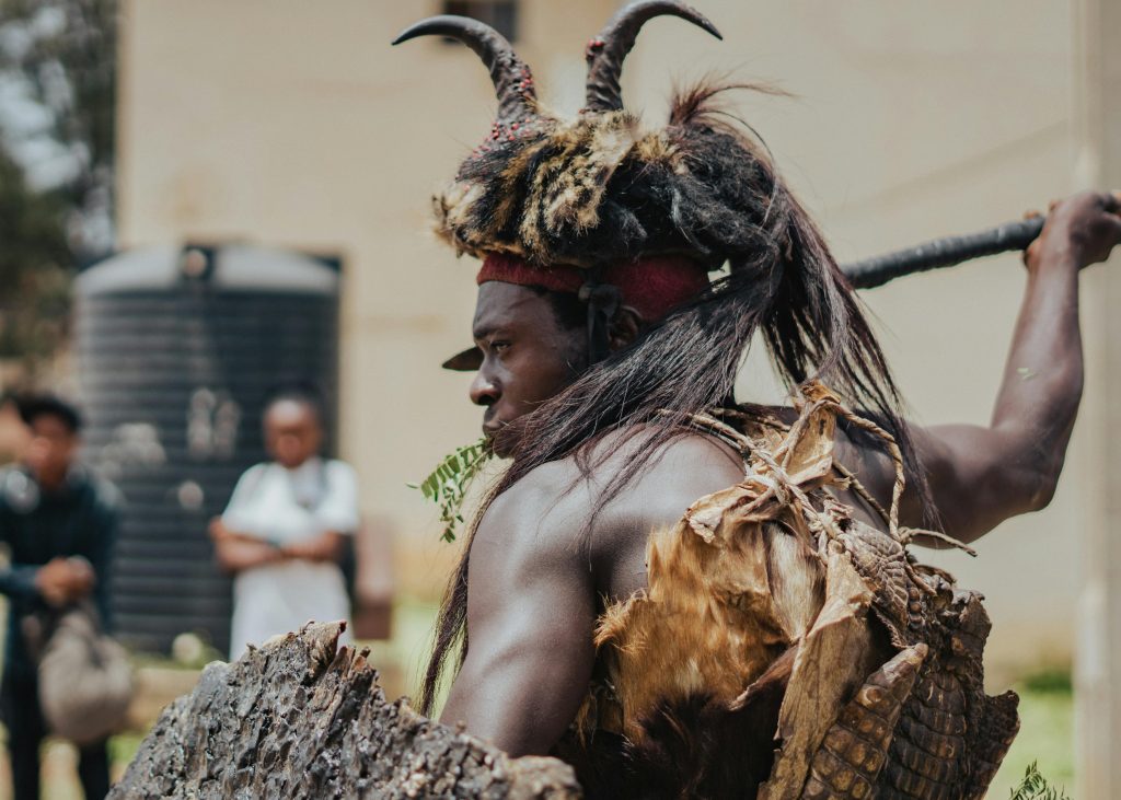 A traditional Nigerian cultural performer wearing an ornate costume with a backdrop of spectators.