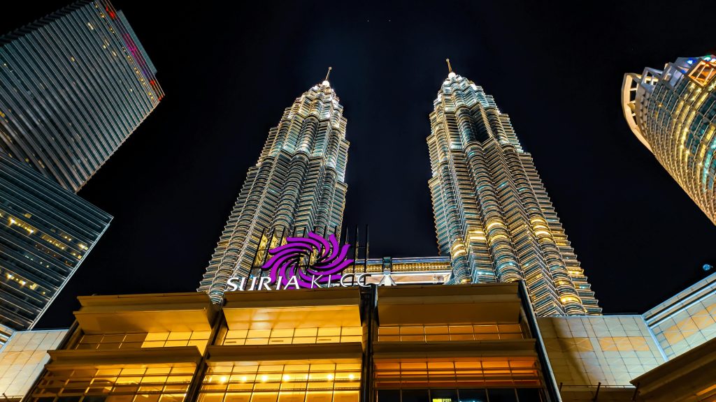 The illuminated Petronas Towers dominate Kuala Lumpur's skyline at night. Stunning low angle view.