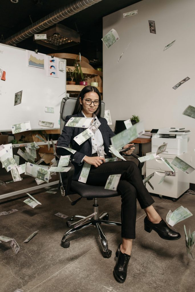 Businesswoman in modern office with falling cash, symbolizing financial success.