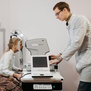 A young girl receives an eye exam from an optician in a clinical setting, focused on vision health.